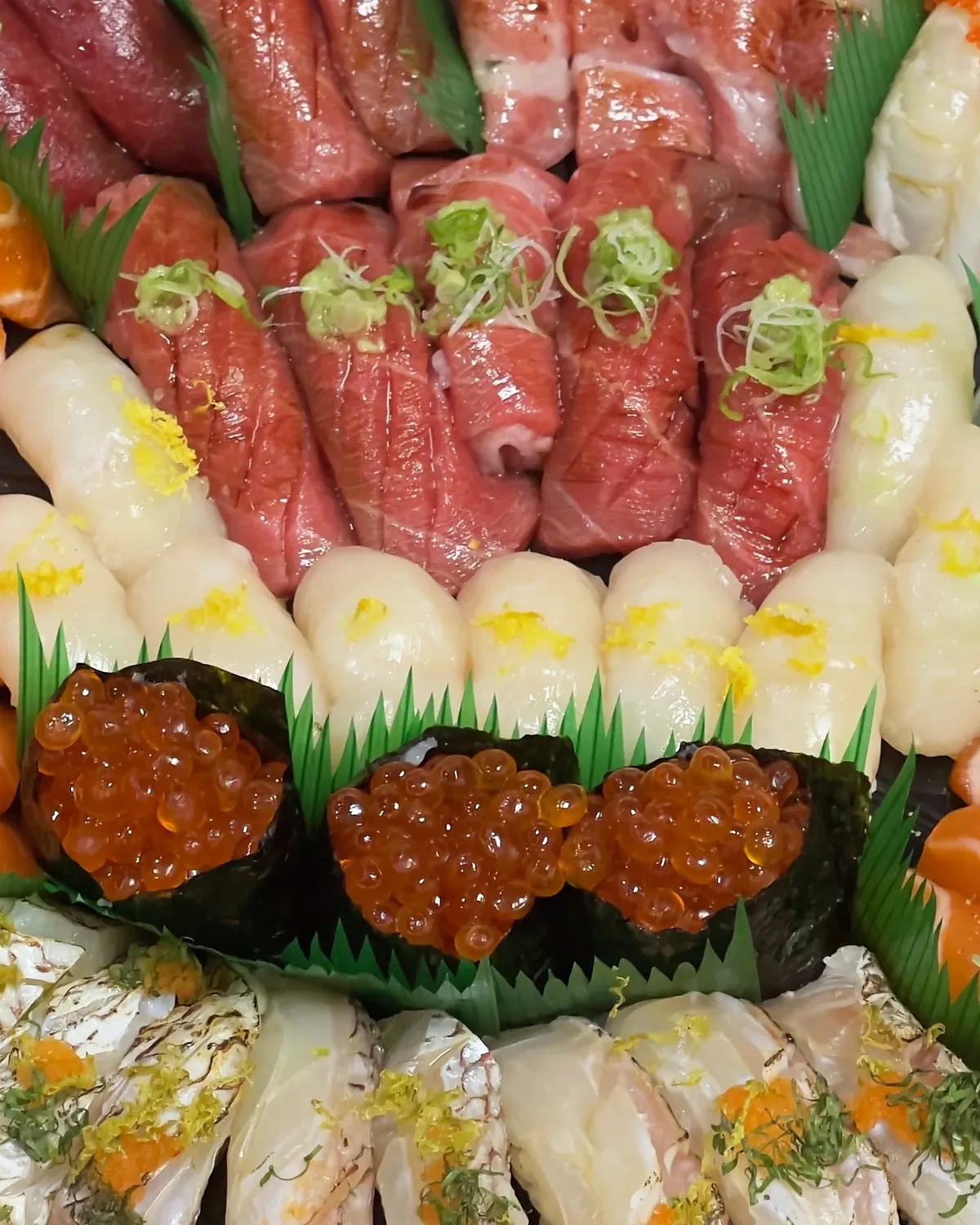 A packed party platter of seared beef, salmon, hamachi and ikura gunkan