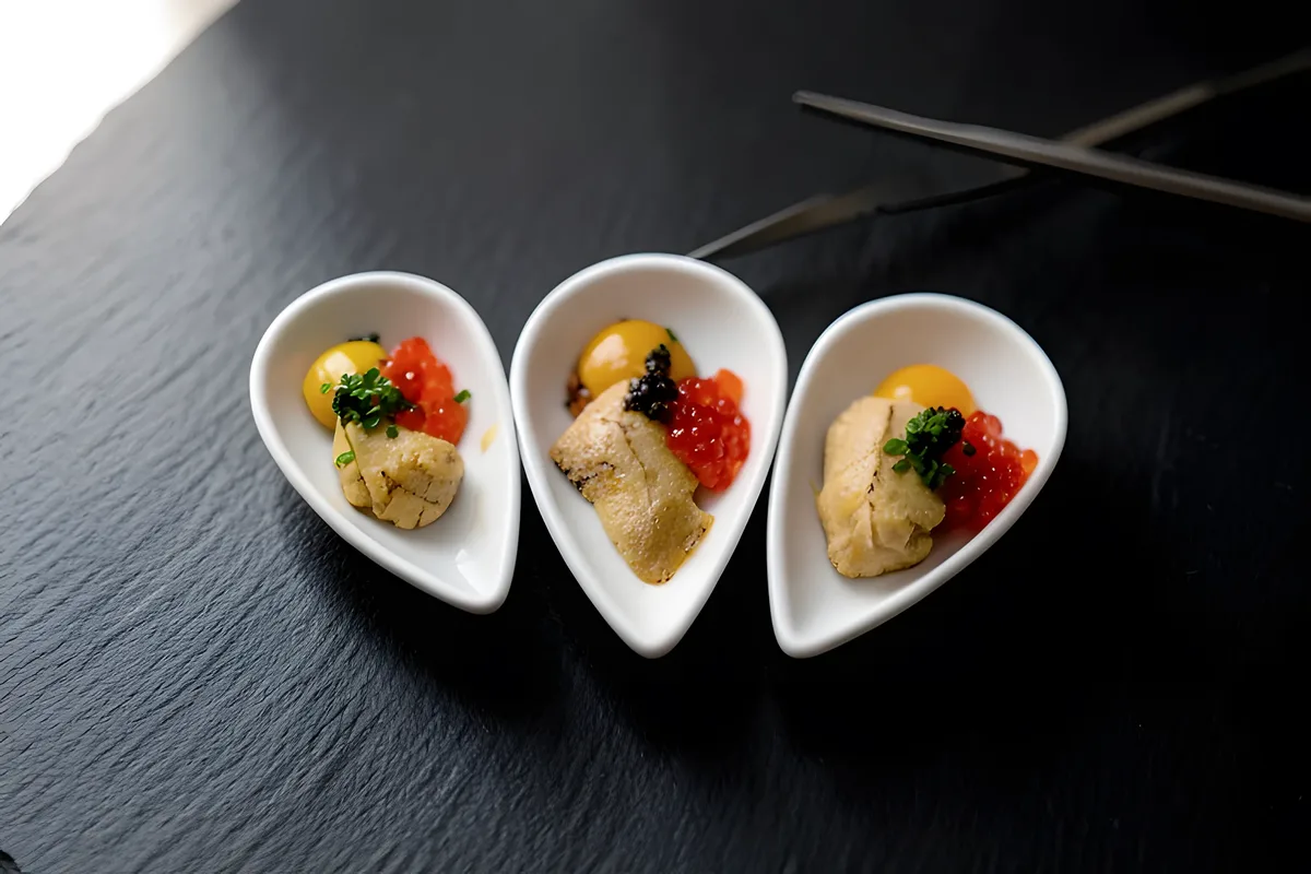 A chef spooning uni and ikura into a line of spoon dishes
