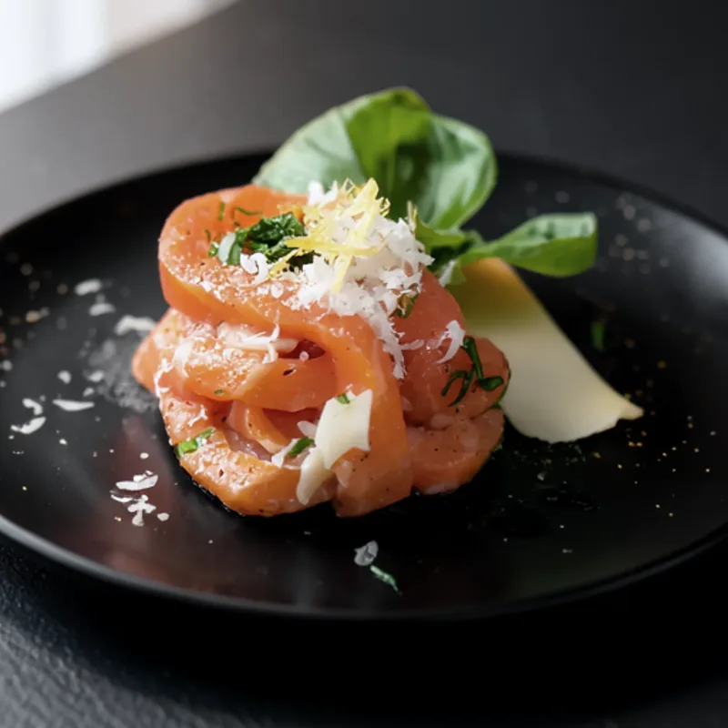 Salmon tartare with cured yolk and shaved cheese on a black plate
