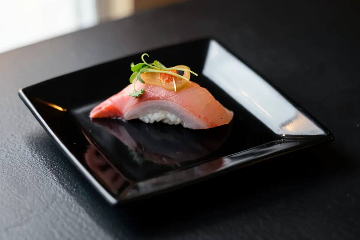 A single piece of fatty tuna nigiri on a black plate beside the knife that cut it
