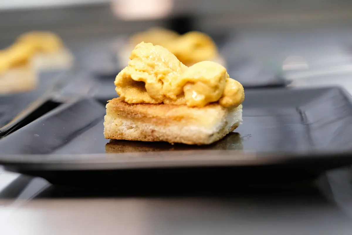 Uni piled on toasted brioche, shot close on a black plate