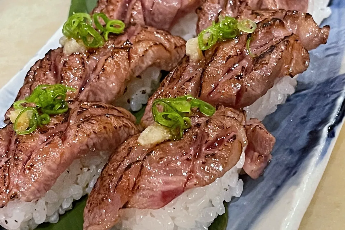 Seared beef nigiri lined up on a blue-and-white plate