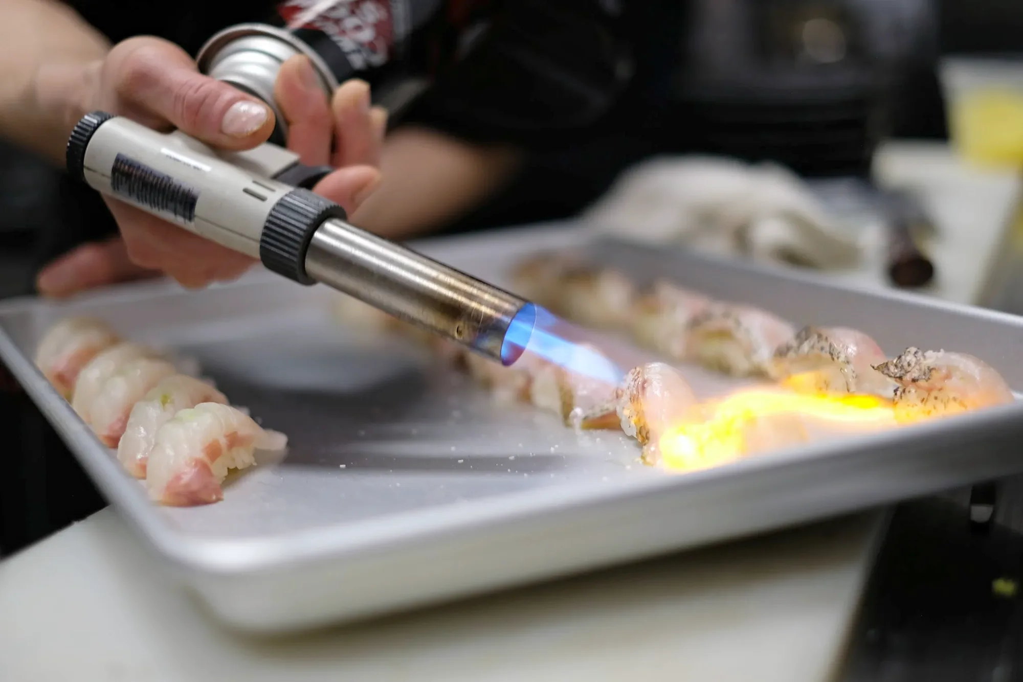 A chef finishing a piece of nigiri under a torch